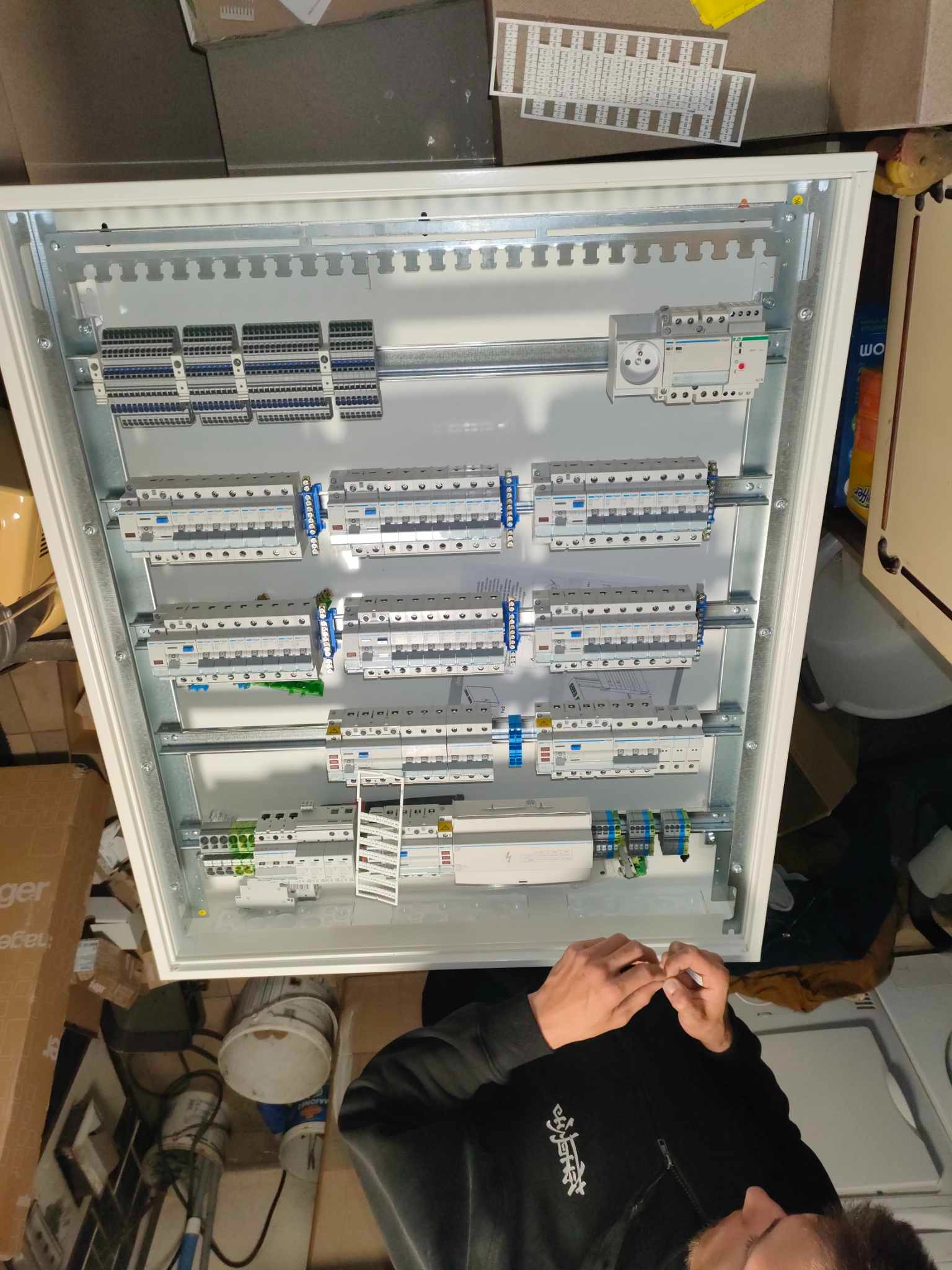 Elektryk w Kacwinie podłącza przewody w rozdzielnicy elektrycznej, widoczne zabezpieczenia nadprądowe i różnicowoprądowe.