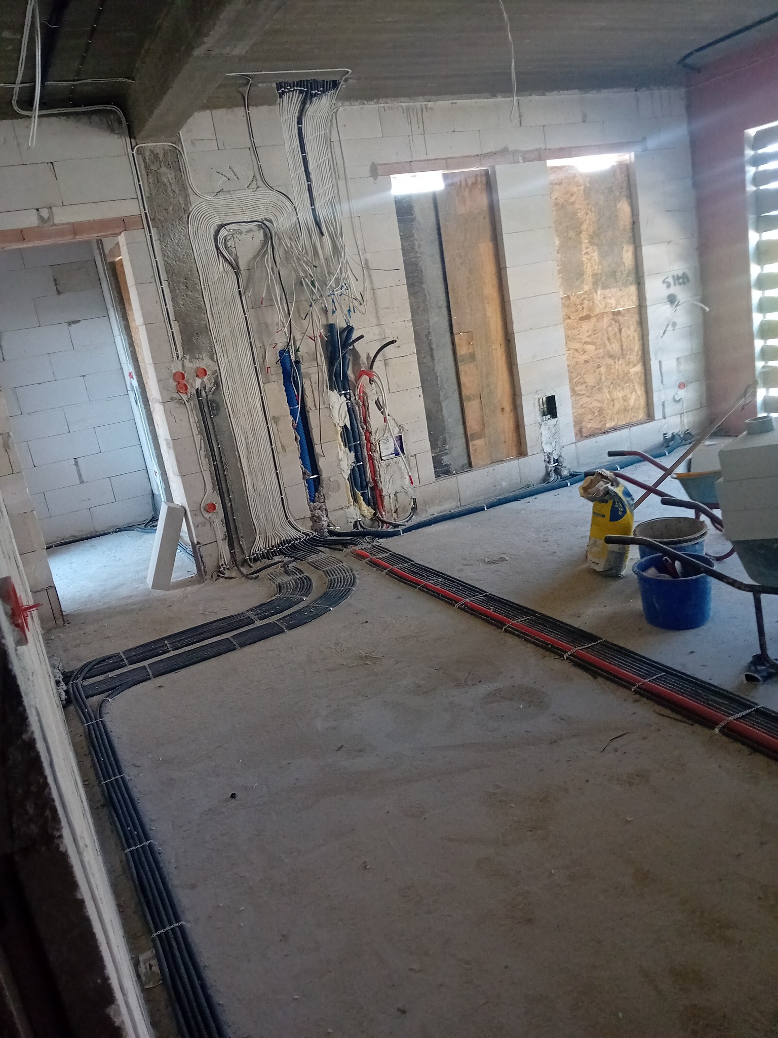 Rozprowadzenie przewodów elektrycznych w surowym budynku, widoczne kable prowadzone po ścianach i podłodze w rurkach ochronnych, przygotowanie do dalszych prac wykończeniowych.