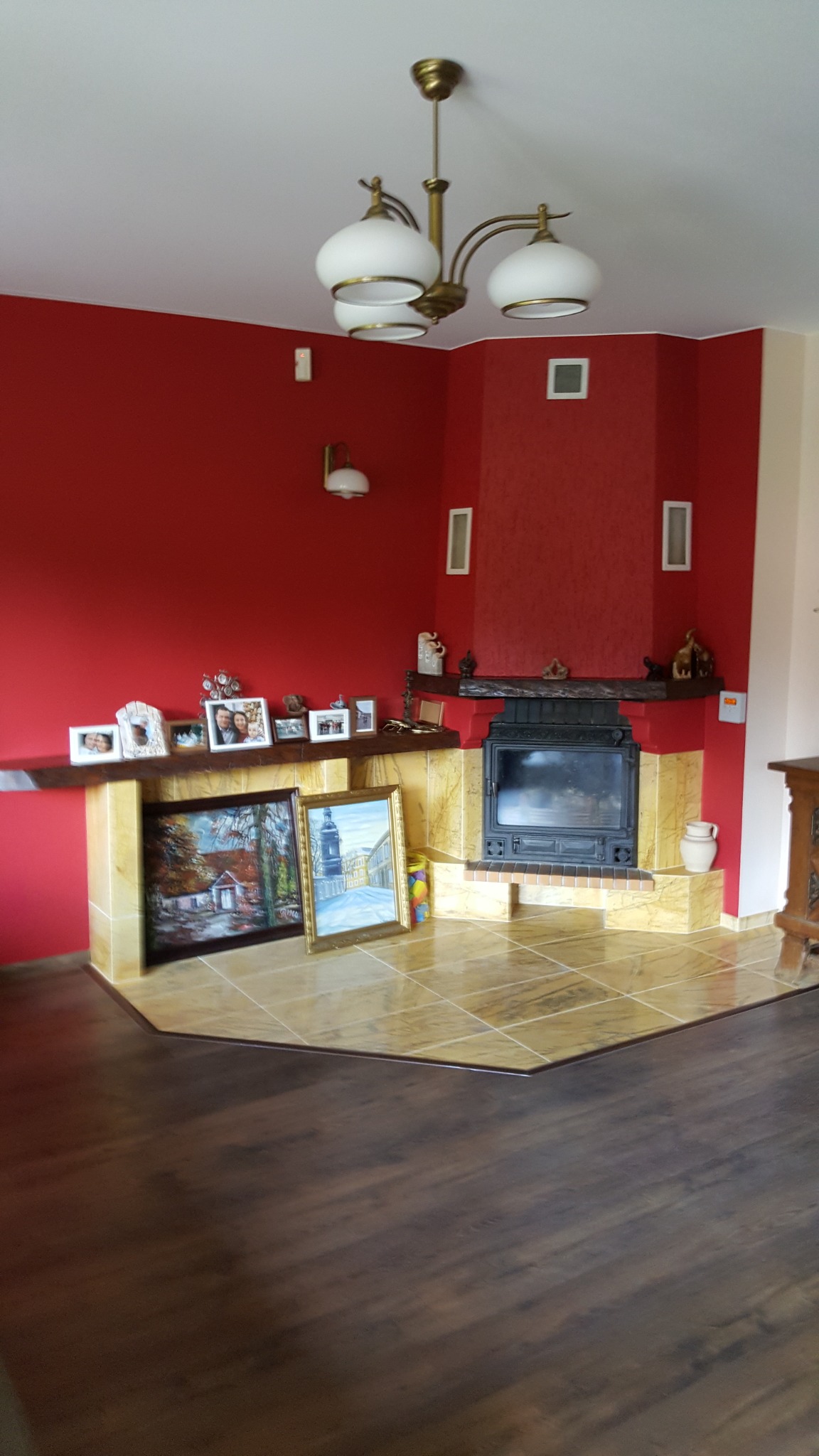 Salon z czerwonymi ścianami, wykończonym kominkiem z marmurową obudową i podłogą, dekoracjami na kominku i obrazami opartymi o ścianę.