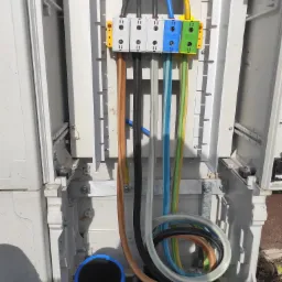 Otwarta skrzynka elektryczna z podłączonymi, kolorowymi przewodami i niebieską rurą karbowaną u dołu