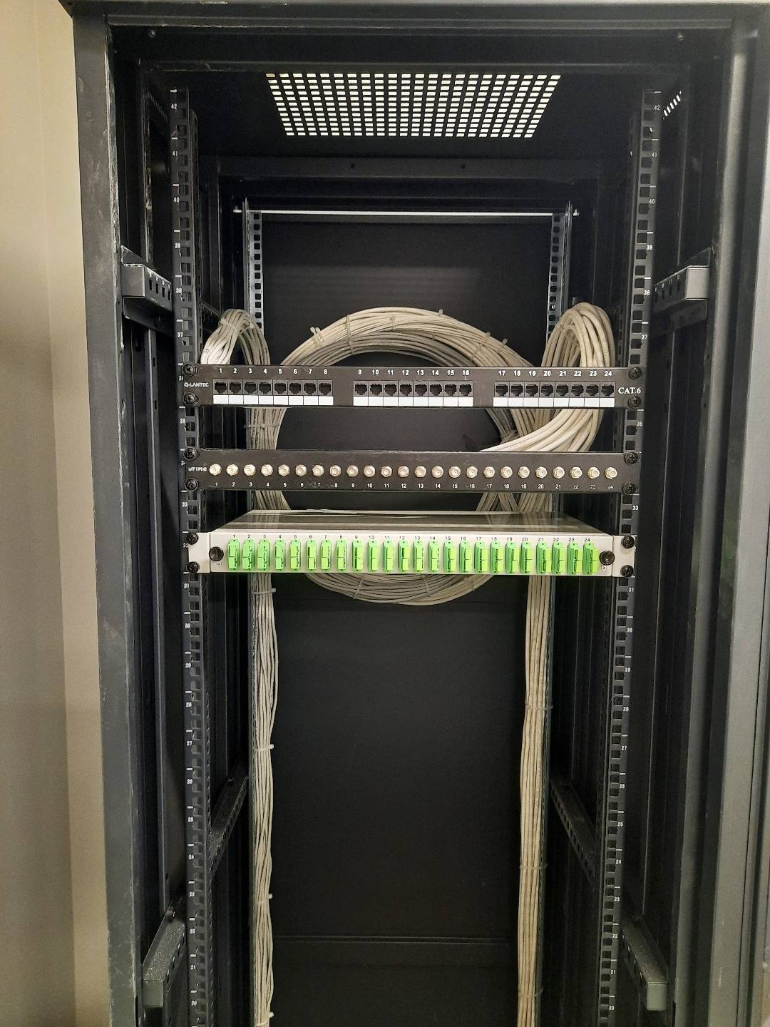 Szafa serwerowa z panelami krosowniczymi i uporządkowanymi kablami CAT6, widok z przodu na czarne wnętrze szafy z uchwytami montażowymi po bokach.