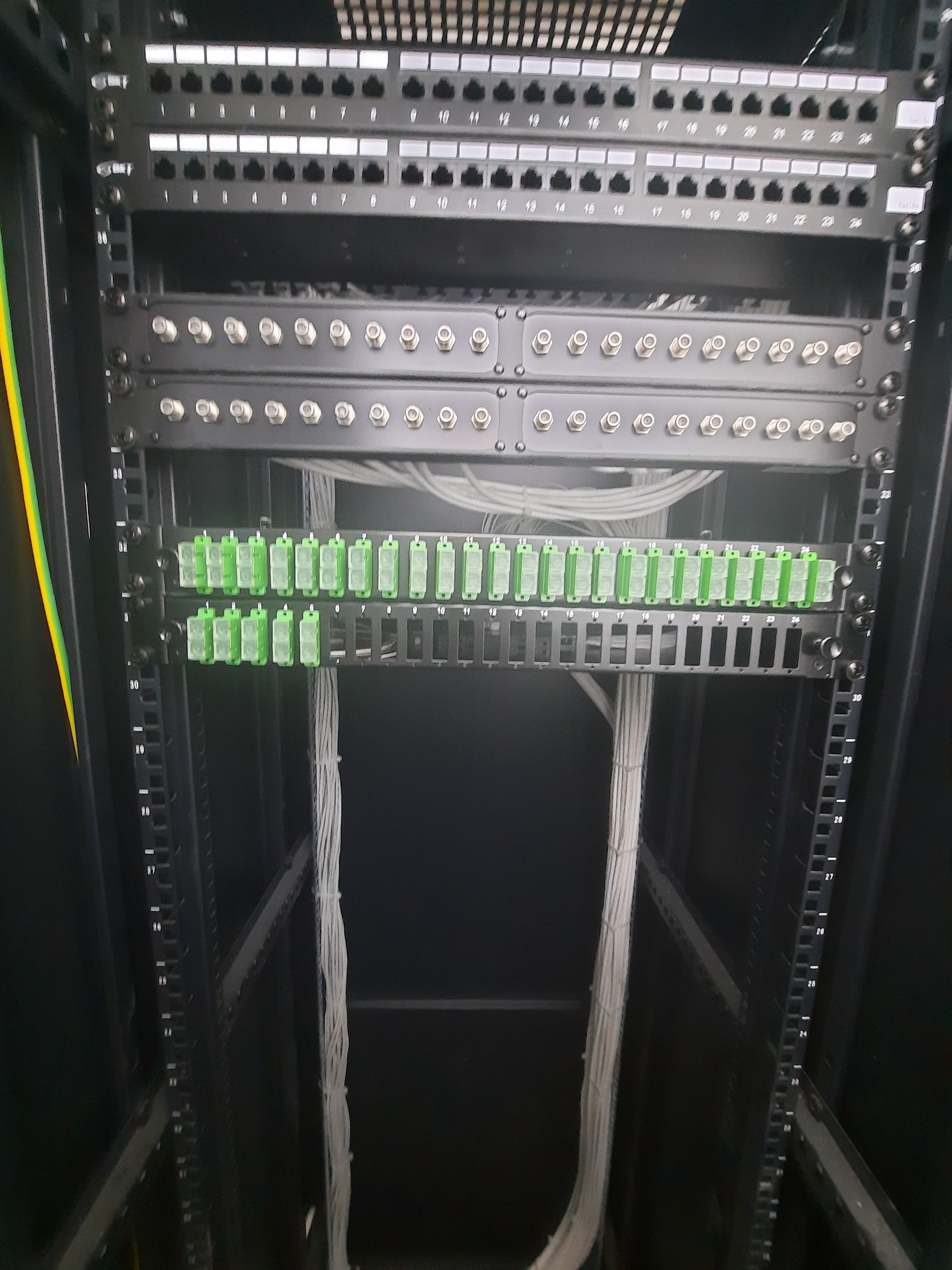 Widok z bliska szafy rack z panelami krosowniczymi, patch panelem z zielonymi wkładkami i uporządkowanymi kablami sieciowymi w serwerowni.