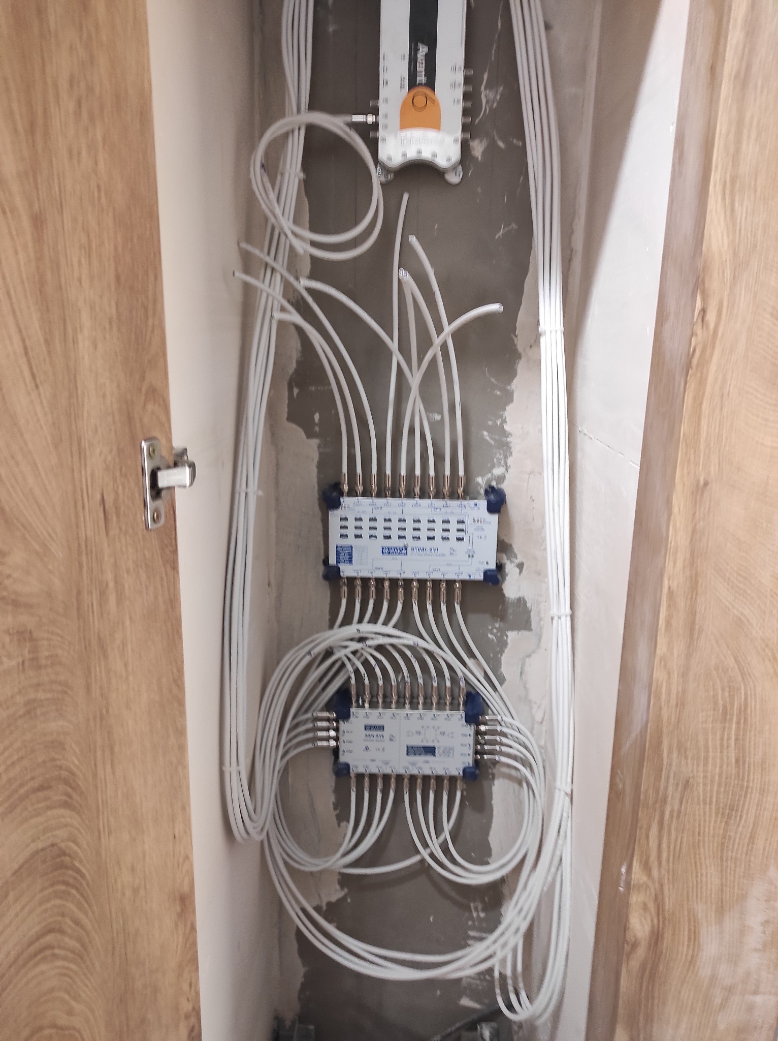 Rozdzielacze sygnału telewizyjnego zamontowane na ścianie w trakcie prac wykończeniowych, widoczne liczne białe kable koncentryczne.