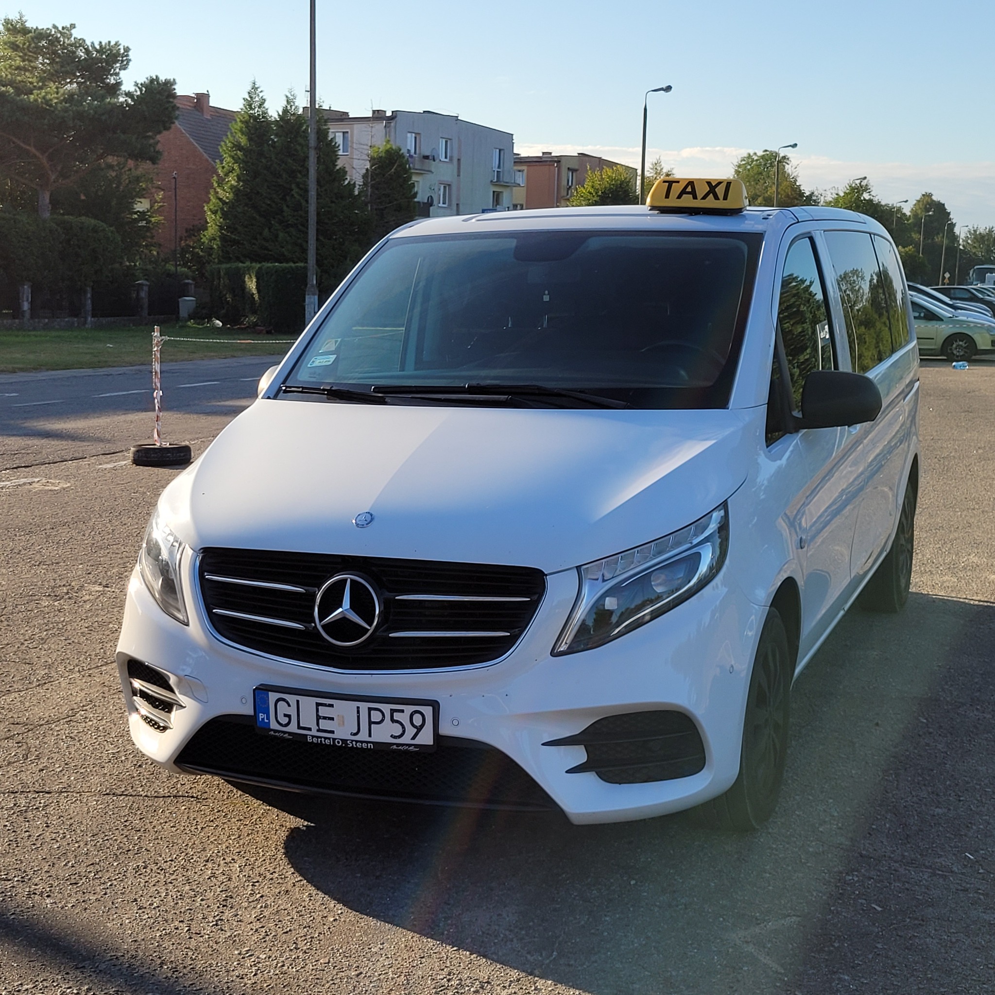 Biały Mercedes-Benz Vito z żółtym oznaczeniem TAXI na dachu, zaparkowany na parkingu w Łebie, widok z przodu.