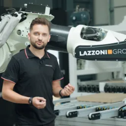 Prezenter w czarnej koszulce z logo firmy na tle nowoczesnego, białego ramienia robota przemysłowego z napisem LAZZONI GROUP.