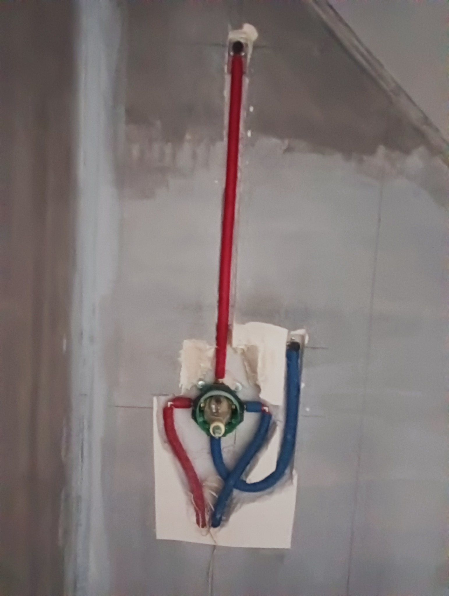 Wnęka w surowej ścianie z widoczną instalacją wodną: czerwone i niebieskie rurki doprowadzające wodę do baterii prysznicowej, zamontowanej w ścianie, przed położeniem płytek.