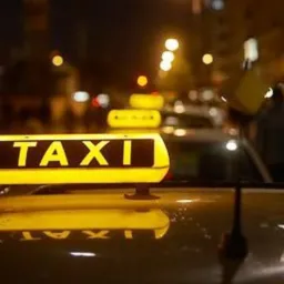 Podświetlony znak TAXI na dachu pojazdu, nocne ujęcie z rozmytym tłem miejskich świateł.