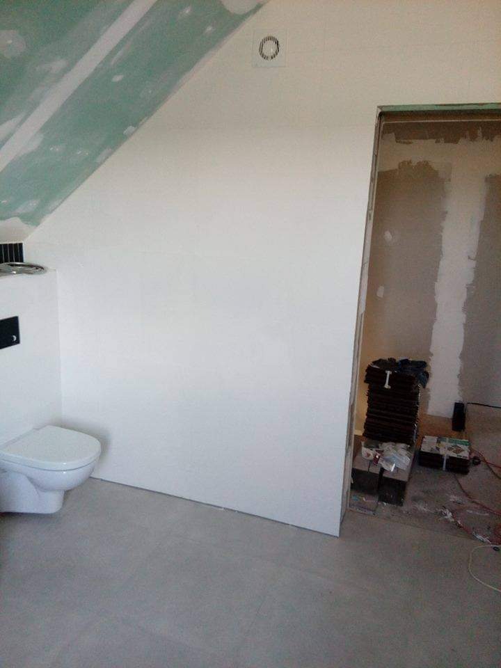 Poddasze ze skośnym sufitem po remoncie, z zamontowaną toaletą i przygotowanym wejściem do innego pomieszczenia, widoczne materiały budowlane.