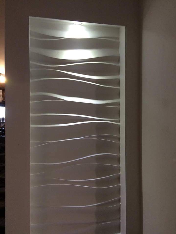 Podświetlona, dekoracyjna ściana z falistym wzorem w korytarzu, oświetlenie punktowe u góry.