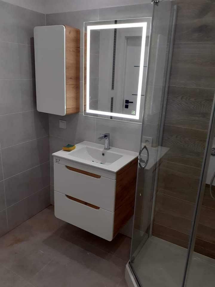 Nowoczesna łazienka z wiszącą szafką z umywalką, podświetlanym lustrem i kabiną prysznicową z przeźroczystego szkła.