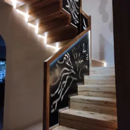 Nowoczesne schody z jasnego drewna z podświetleniem LED i metalową balustradą z wycinanym wzorem abstrakcyjnym.