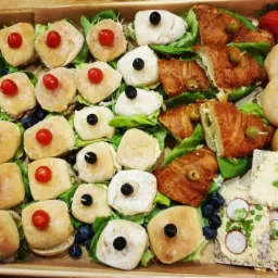 Drewniana taca z r&oacute;żnorodnymi przekąskami: mini bułeczki z pomidorkami i oliwkami, croissanty z farszem, bajgle, krakersy z pastą i rzodkiewką, udekorowane sałatą i bor&oacute;wkami.