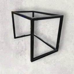 Stalowa konstrukcja stołu z profili kwadratowych, spawana, czarna, na tle szarej, betonowej ściany.