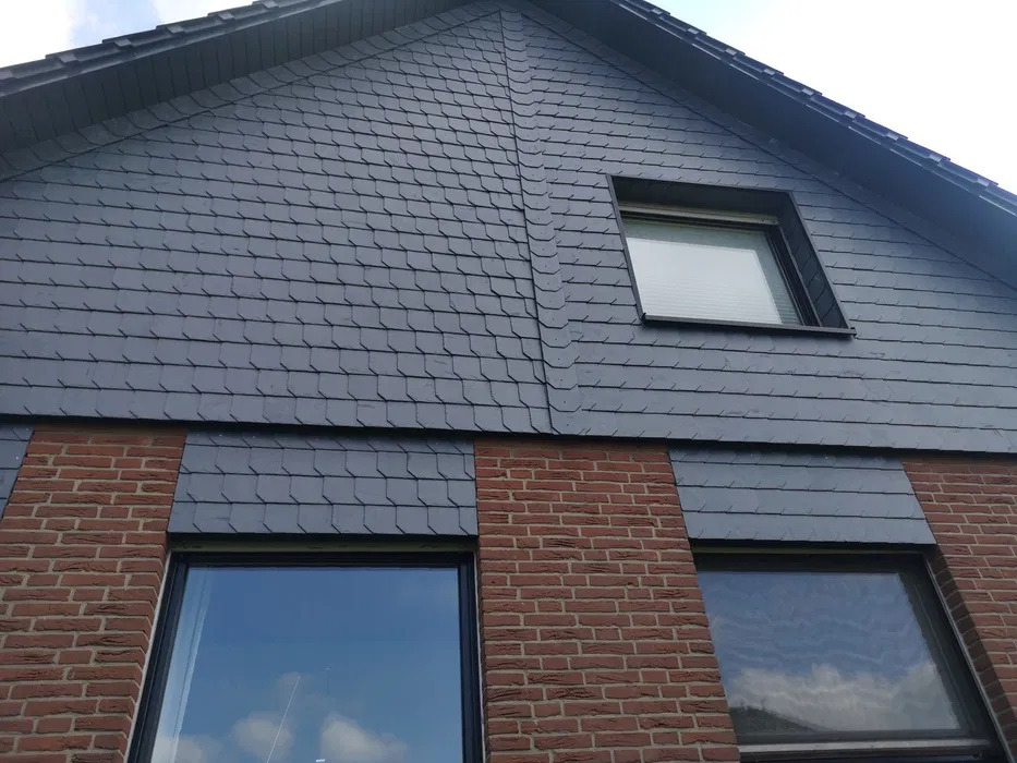 Fragment elewacji domu z szarym łupkiem i czerwoną cegłą, widoczne okna z odbiciem nieba.