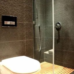 Nowoczesna łazienka z ciemnymi, wzorzystymi płytkami, podwieszaną toaletą i kabiną prysznicową z drewnianym rusztem podłogowym.