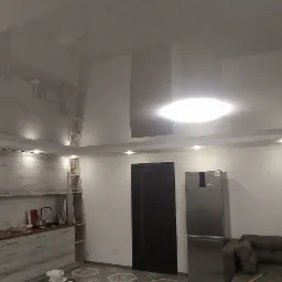 Błyszczący, lakierowany sufit z wbudowanym oświetleniem punktowym w nowoczesnym salonie z aneksem kuchennym, odbijający światło i elementy wyposażenia.