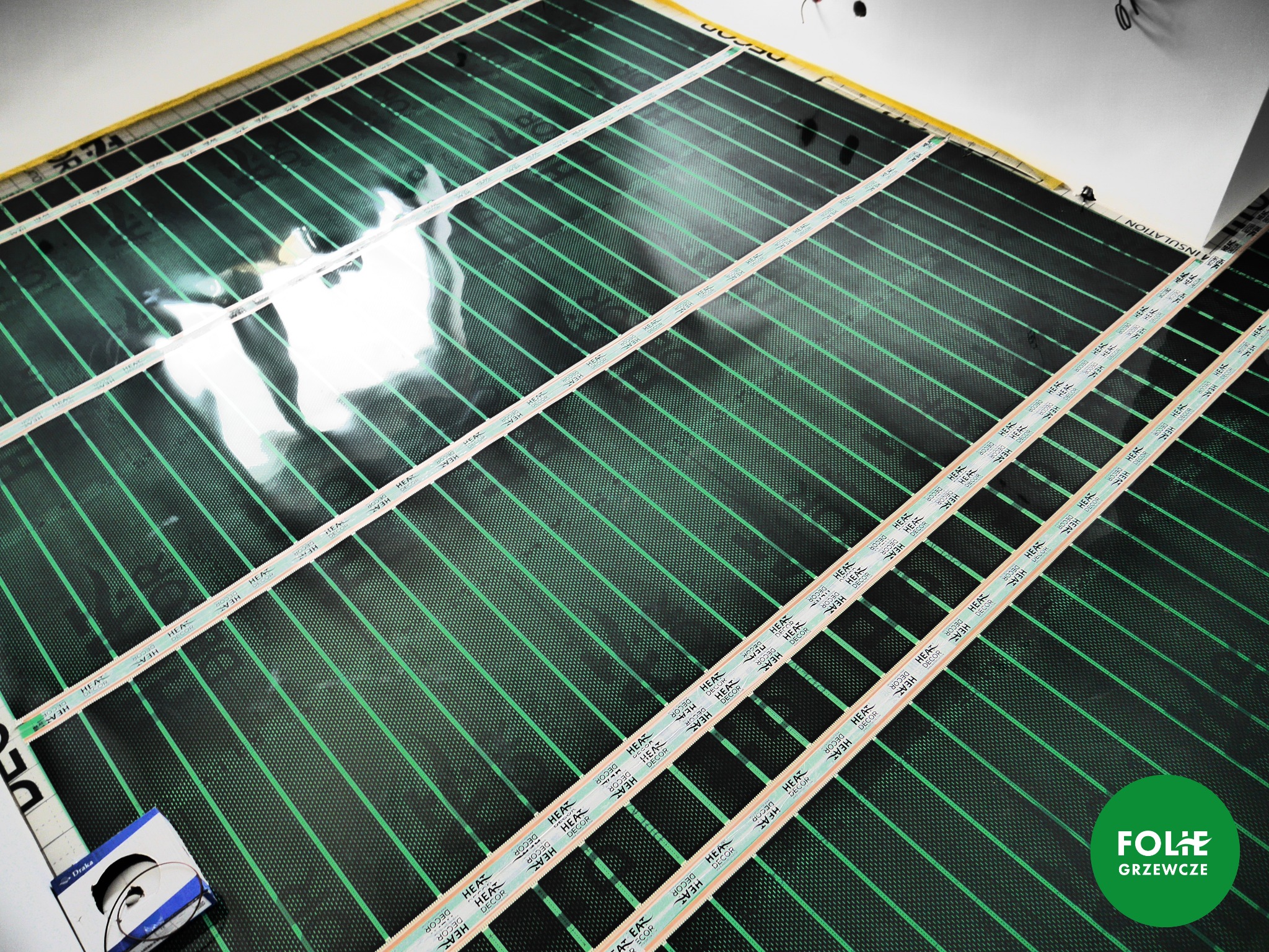 Rozłożona mata grzewcza z widocznymi paskami montażowymi i elementami grzejnymi, przygotowana do instalacji pod podłogę.