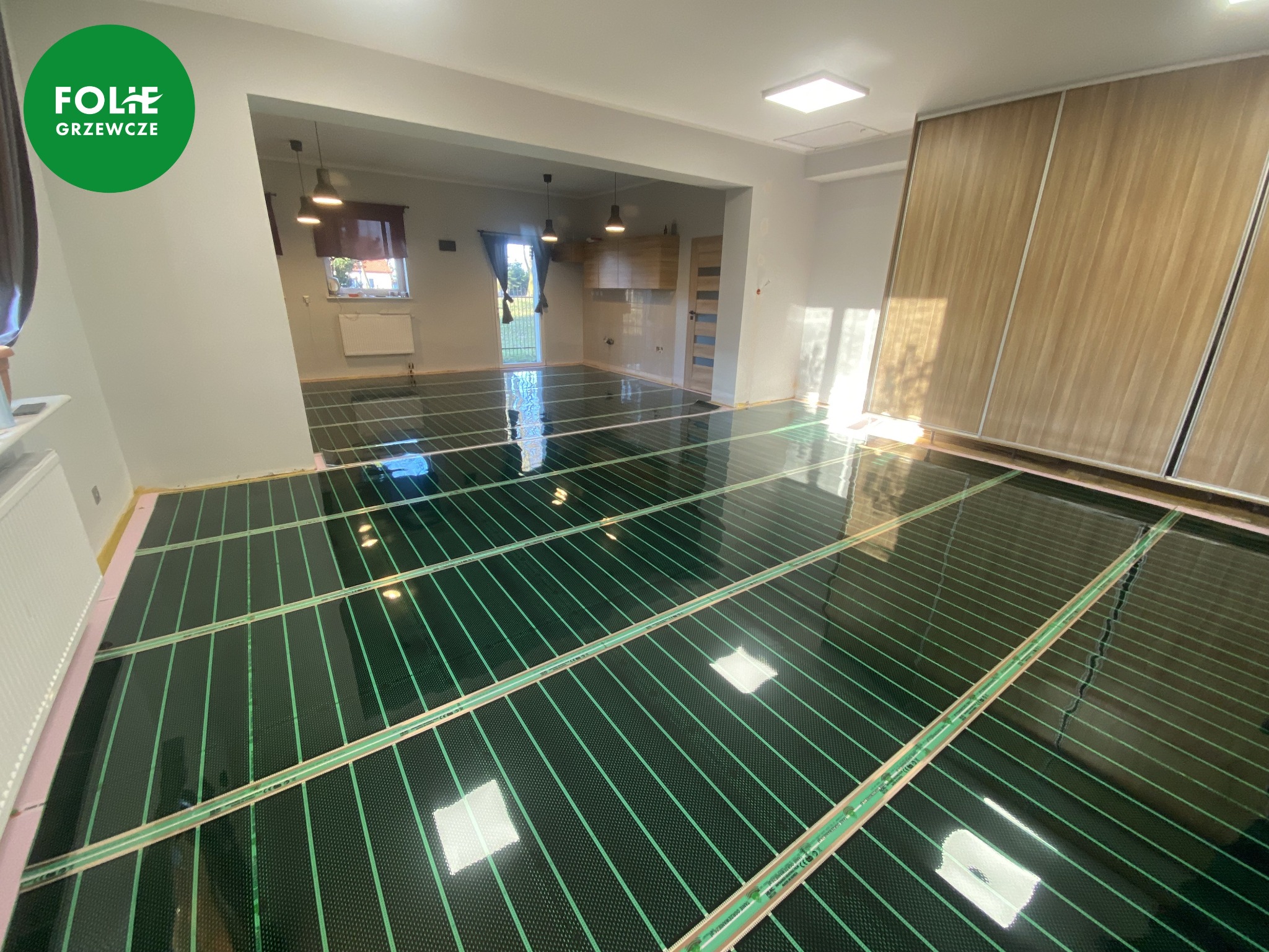 Rozłożone maty grzewcze pod ogrzewanie podłogowe, widoczna struktura folii z zielonymi paskami grzewczymi, przygotowane do dalszych prac wykończeniowych.