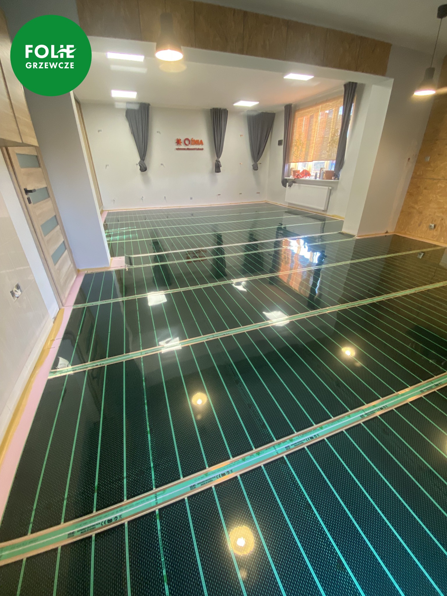 Rozłożone maty grzewcze na podłodze w jasnym pomieszczeniu, widoczna izolacja po bokach, przygotowane do dalszych prac wykończeniowych.