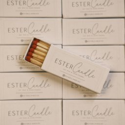 Nadya_Kova Photo - Stos pudełek z sojowymi świecami 'Ester Candle' z dopasowanymi zapałkami na wierzchu, prezentacja produktu.