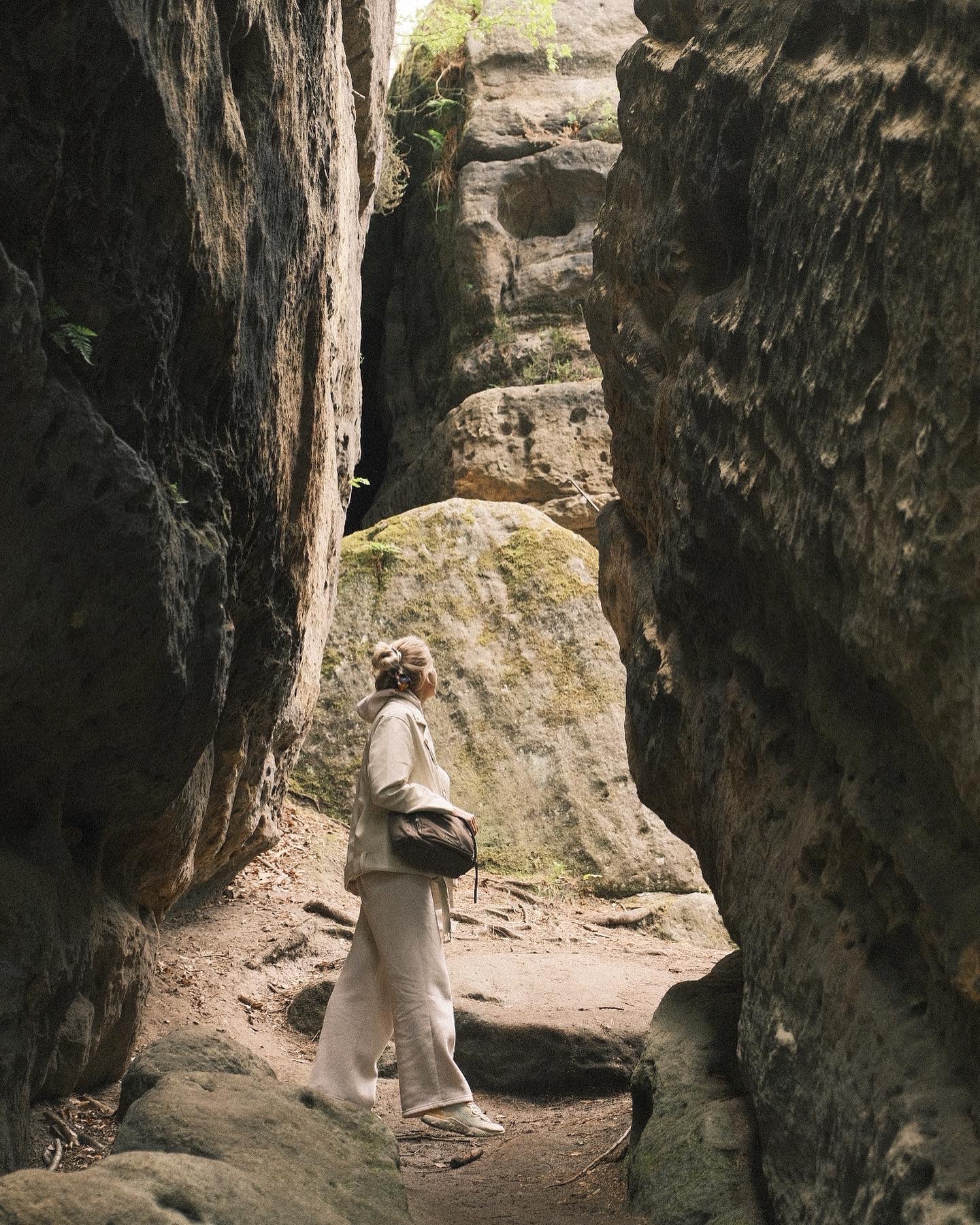 Kobieta w jasnym stroju spaceruje wąskim przesmykiem między wysokimi, skalistymi ścianami w naturalnym otoczeniu.