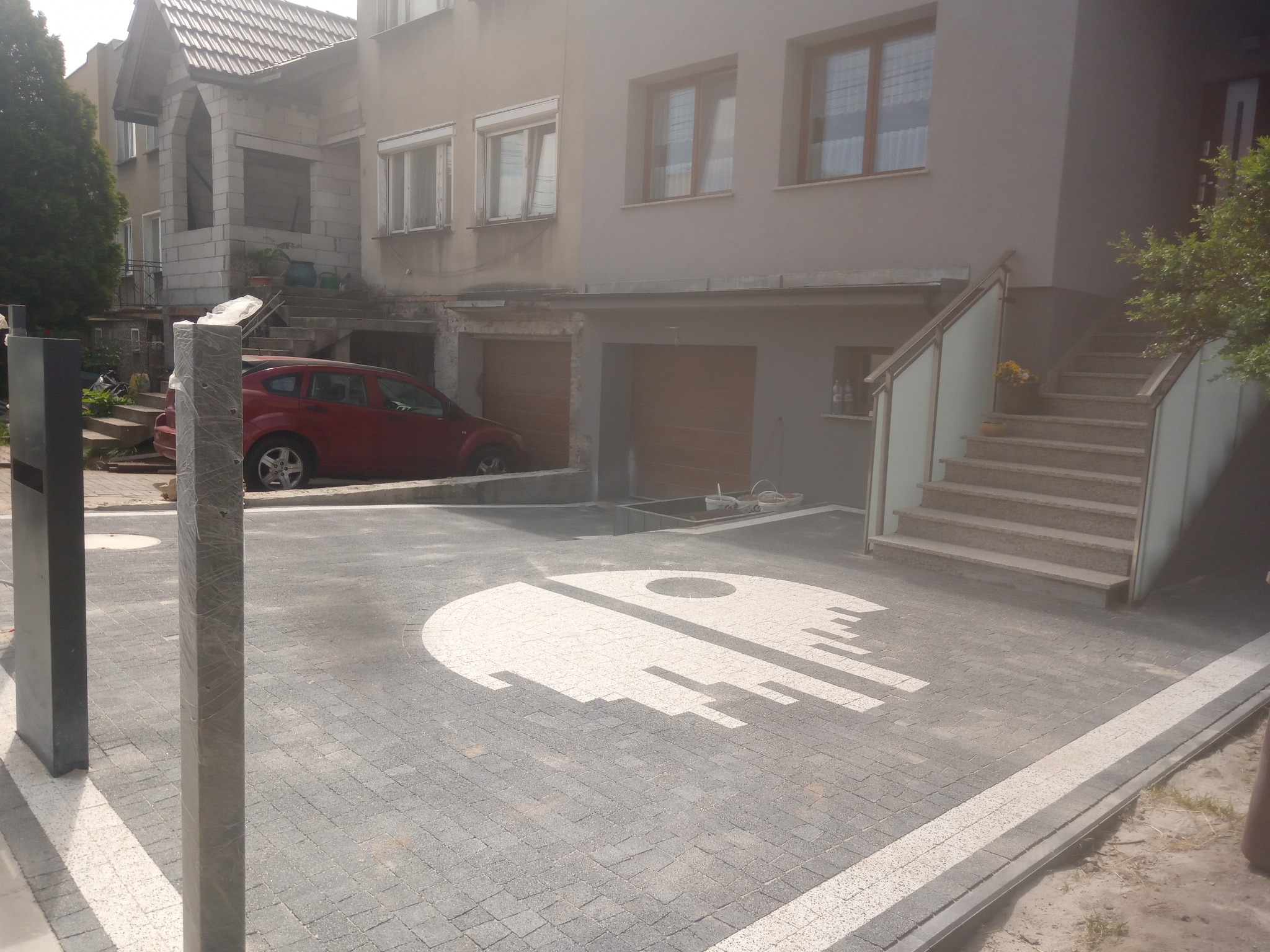 Ułożona kostka brukowa przed domem z motywem białej Gwiazdy Śmierci. Widoczne dwa słupki z przodu i czerwony samochód w tle.