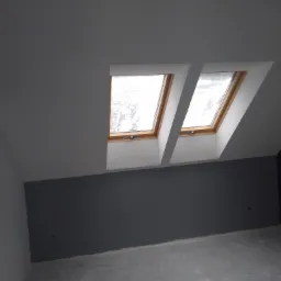 Poddasze po remoncie z dwoma oknami dachowymi, ściany pomalowane na dwa kolory: biały i szary, surowa podłoga betonowa.