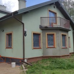 Jabud - Dwupiętrowy dom z balkonem w trakcie prac elewacyjnych, okna zabezpieczone folią, widoczny numer domu '6' oraz częściowo nałożona warstwa szarej zaprawy.