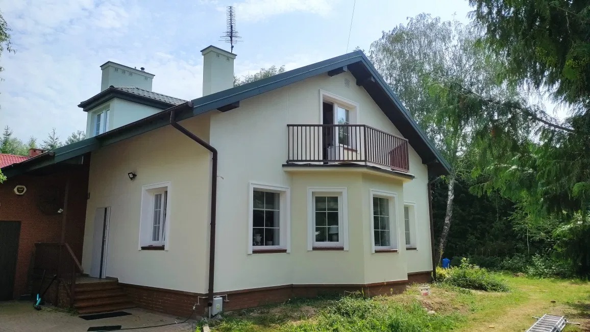 Dom jednorodzinny po remoncie elewacji, z balkonem z czarną balustradą, widok z ogrodu w słoneczny dzień.