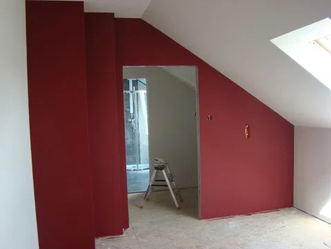 Pokój na poddaszu z pomalowanymi na bordowo ścianami, widoczna drabina i otwór drzwiowy do łazienki z prysznicem.