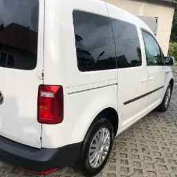 Biały samochód dostawczy Volkswagen Caddy po umyciu, zaparkowany na kostce brukowej, z widocznymi kroplami wody na oponach i karoserii.