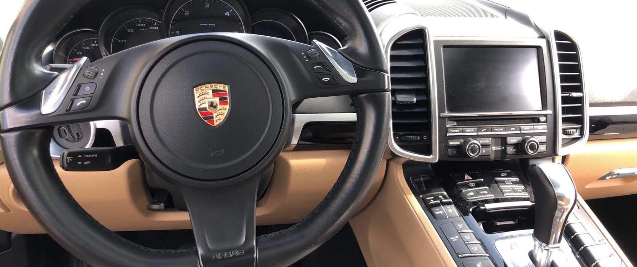 Wnętrze samochodu marki Porsche z widoczną kierownicą z logo, deską rozdzielczą i elementami wykończenia w kolorze beżowym.