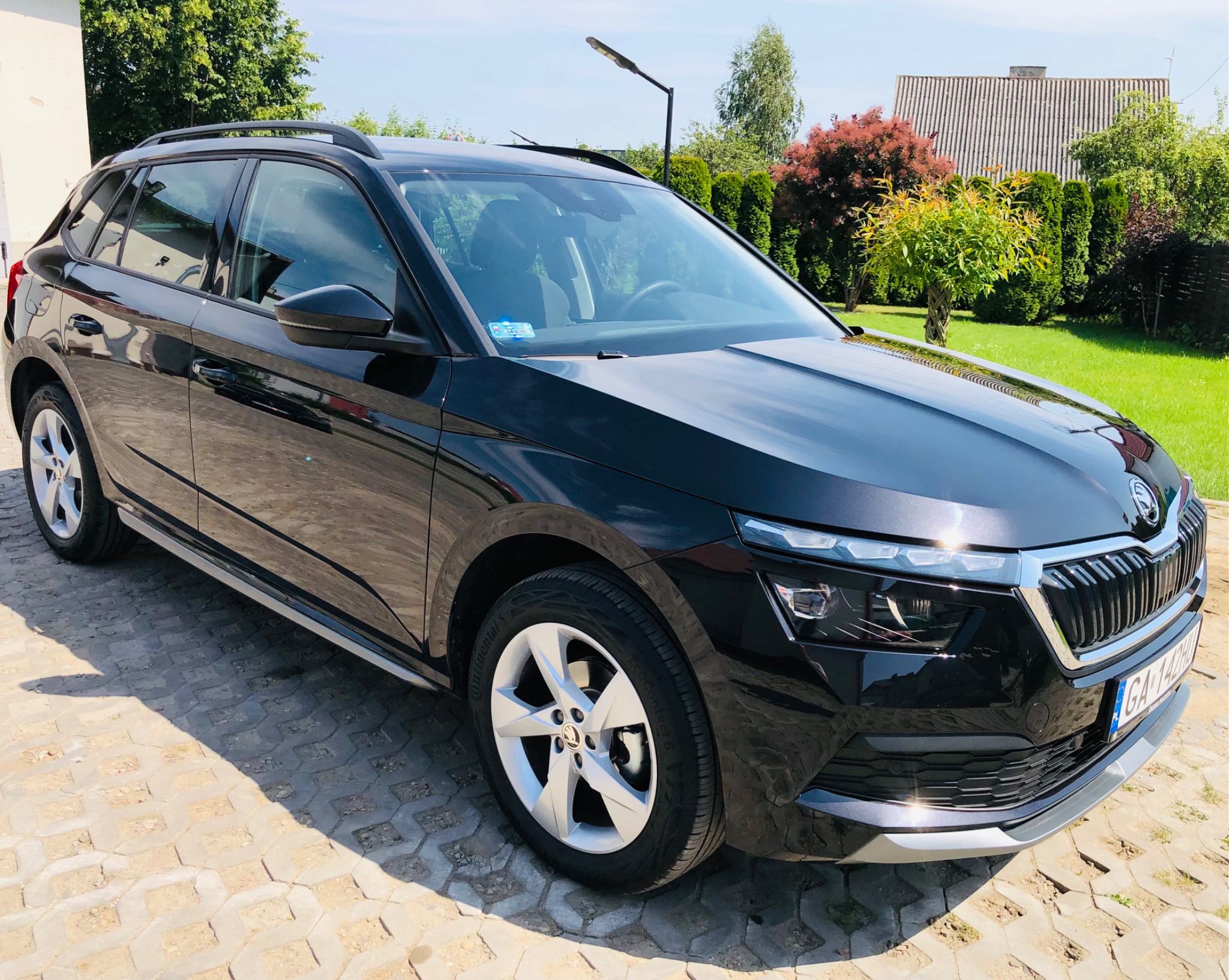 Wypolerowany, czarny samochód Skoda Kamiq zaparkowany na kostce brukowej, z widocznymi detalami karoserii i otaczającą zielenią.