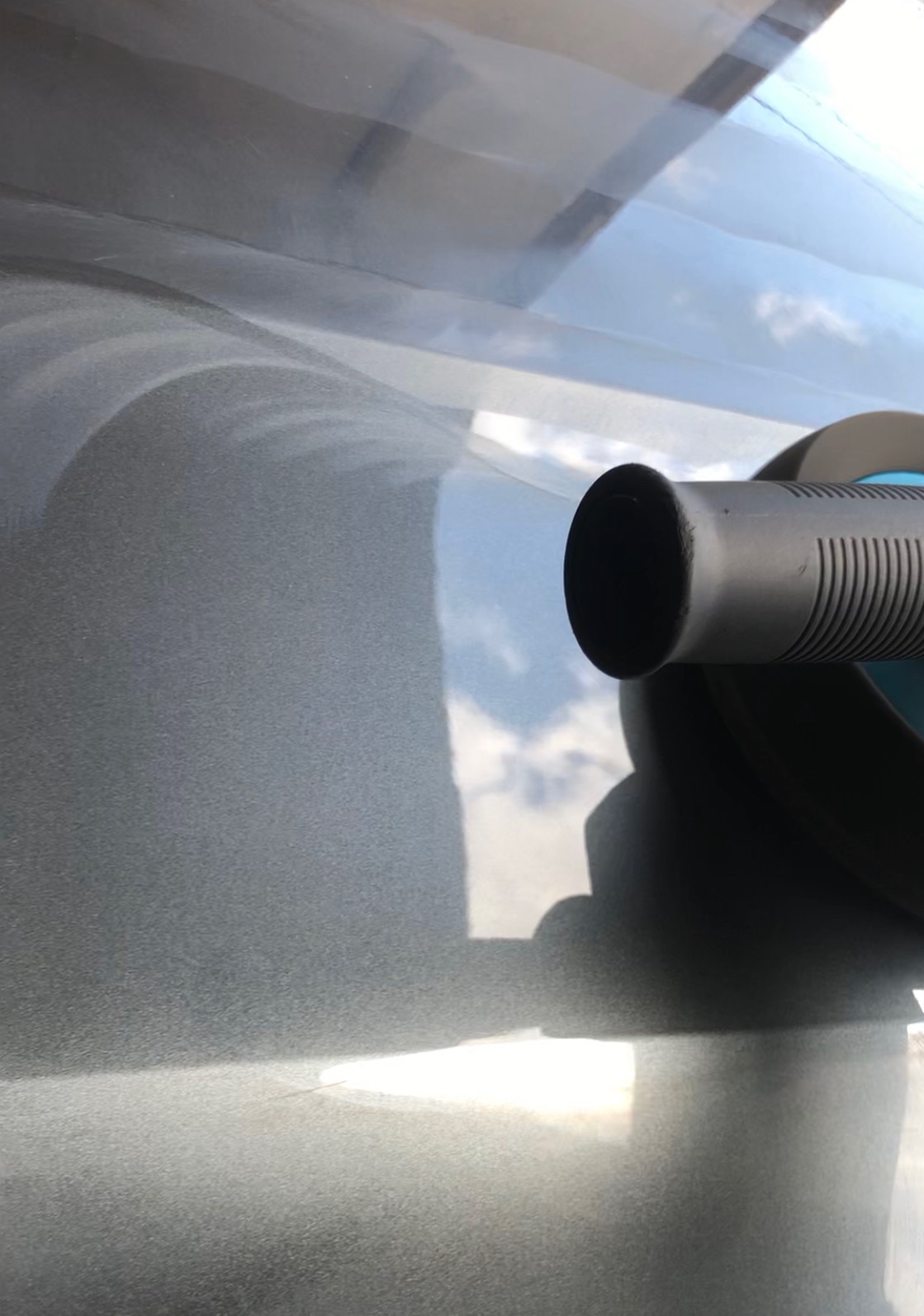 Polerowanie lakieru samochodowego za pomocą elektrycznej polerki, widoczne odbicie nieba w lśniącej powierzchni.