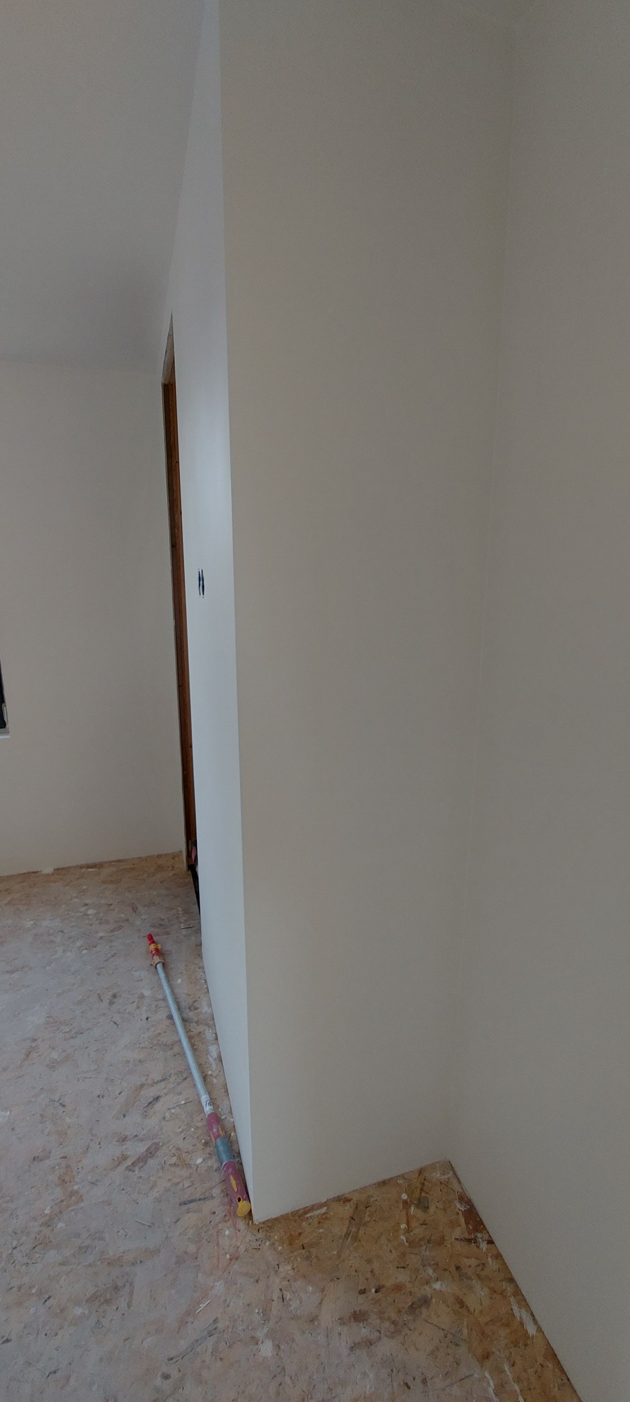Świeżo pomalowany narożnik pokoju z widocznym wałkiem do malowania opartym o ścianę i surową podłogę.