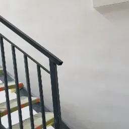 Świeżo otynkowana ściana klatki schodowej z widocznymi schodami zabezpieczonymi folią malarską, w tle biały grzejnik.