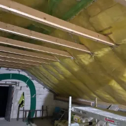 Ocieplenie poddasza wełną mineralną, widoczne krokwie, rusztowanie i rury wentylacyjne.