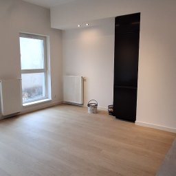 URB GROUP SPÓŁKA Z OGRANICZONĄ ODPOWIEDZIALNOŚCIĄ - Jasne panele podłogowe w nowym wnętrzu z grzejnikami i nowoczesnym oświetleniem sufitowym. Widoczne wiaderka po farbie.
