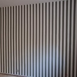 URB GROUP SPÓŁKA Z OGRANICZONĄ ODPOWIEDZIALNOŚCIĄ - Ściana w pokoju po malowaniu w pionowe, szare pasy. Widoczne narzędzia malarskie przy oknie. Wykończenie wnętrz w nowoczesnym stylu.