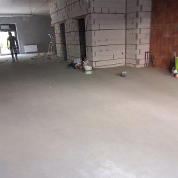 URB GROUP SPÓŁKA Z OGRANICZONĄ ODPOWIEDZIALNOŚCIĄ - Surowy stan wnętrza z blokami betonu komórkowego tworzącymi ściany działowe, widoczne instalacje i pracownik w tle, przygotowanie do dalszych prac wykończeniowych.