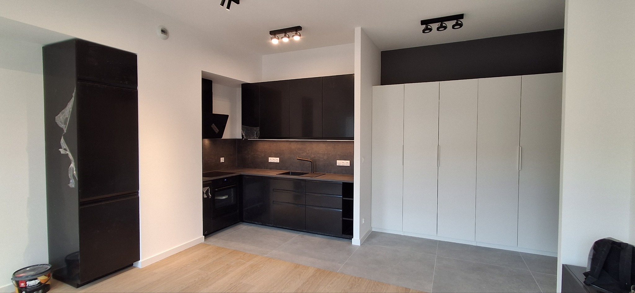 Nowoczesna kuchnia w odcieniach szarości i czerni z oświetleniem punktowym. Minimalistyczny design, zabudowa kuchenna z matowymi frontami i szara podłoga.