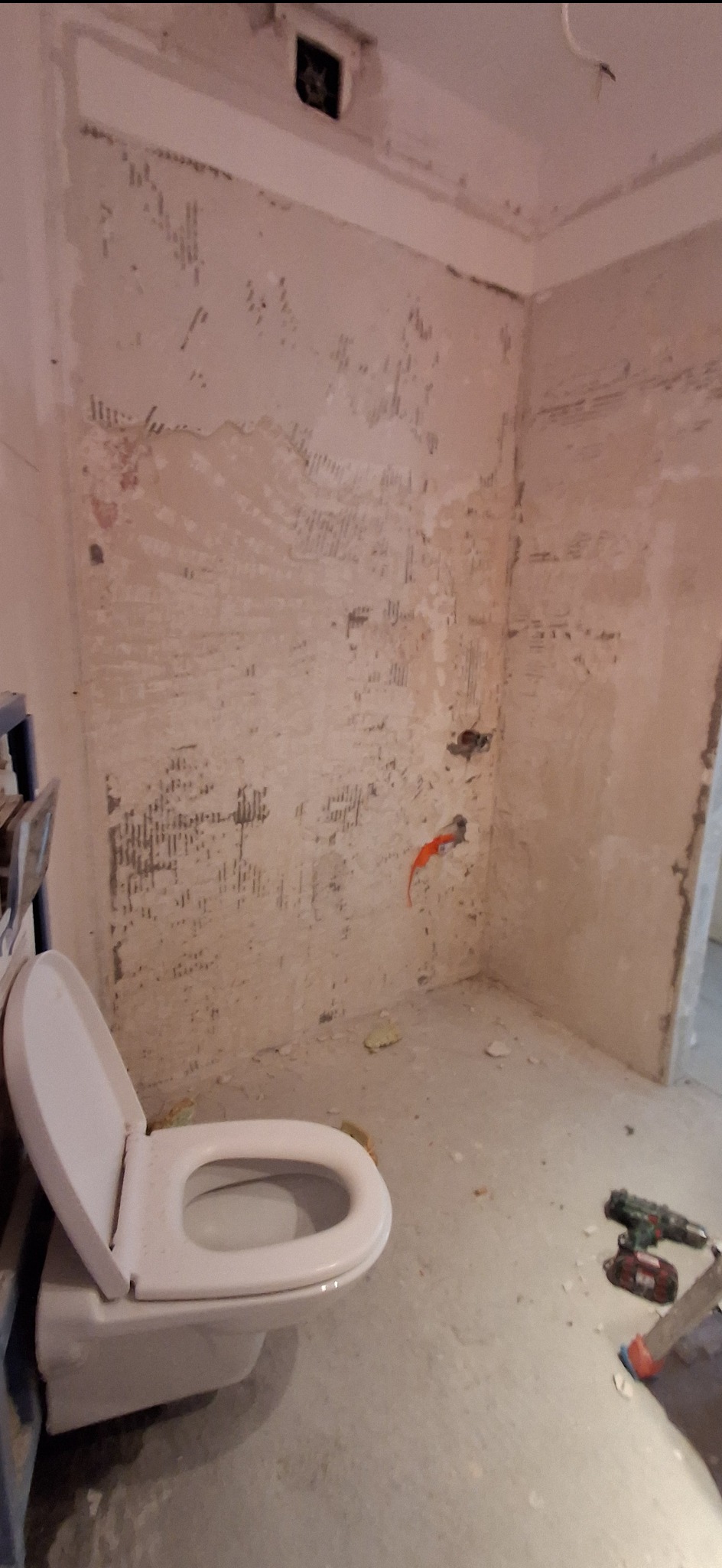 Łazienka w trakcie remontu: widoczne ślady po skuciu płytek na ścianach, wisząca toaleta i narzędzia na podłodze. Przygotowanie do dalszych prac wykończeniowych.