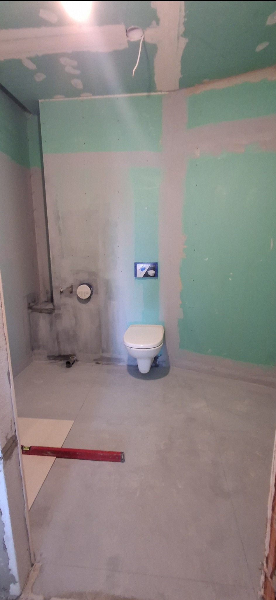 Wnętrze łazienki w trakcie prac w Poznaniu. Widoczne płyty karton-gips na ścianach, zamontowana toaleta i poziomica na podłodze. Etap przygotowania do dalszych prac.