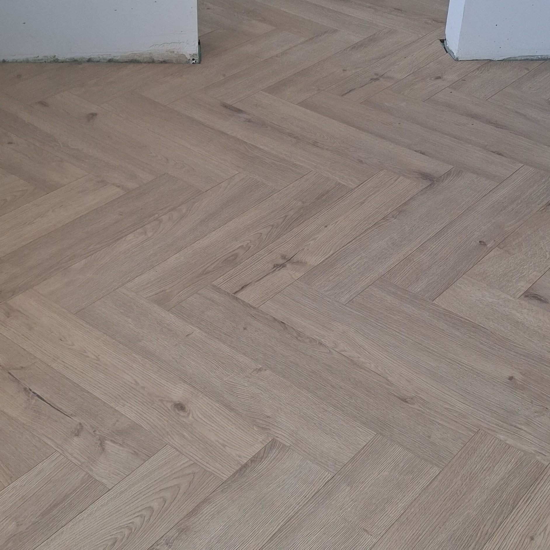 Ułożona podłoga z paneli w jodełkę francuską, jasne odcienie drewna, widoczne fragmenty ścian. Nowoczesne wykończenie podłogi w mieszkaniu.