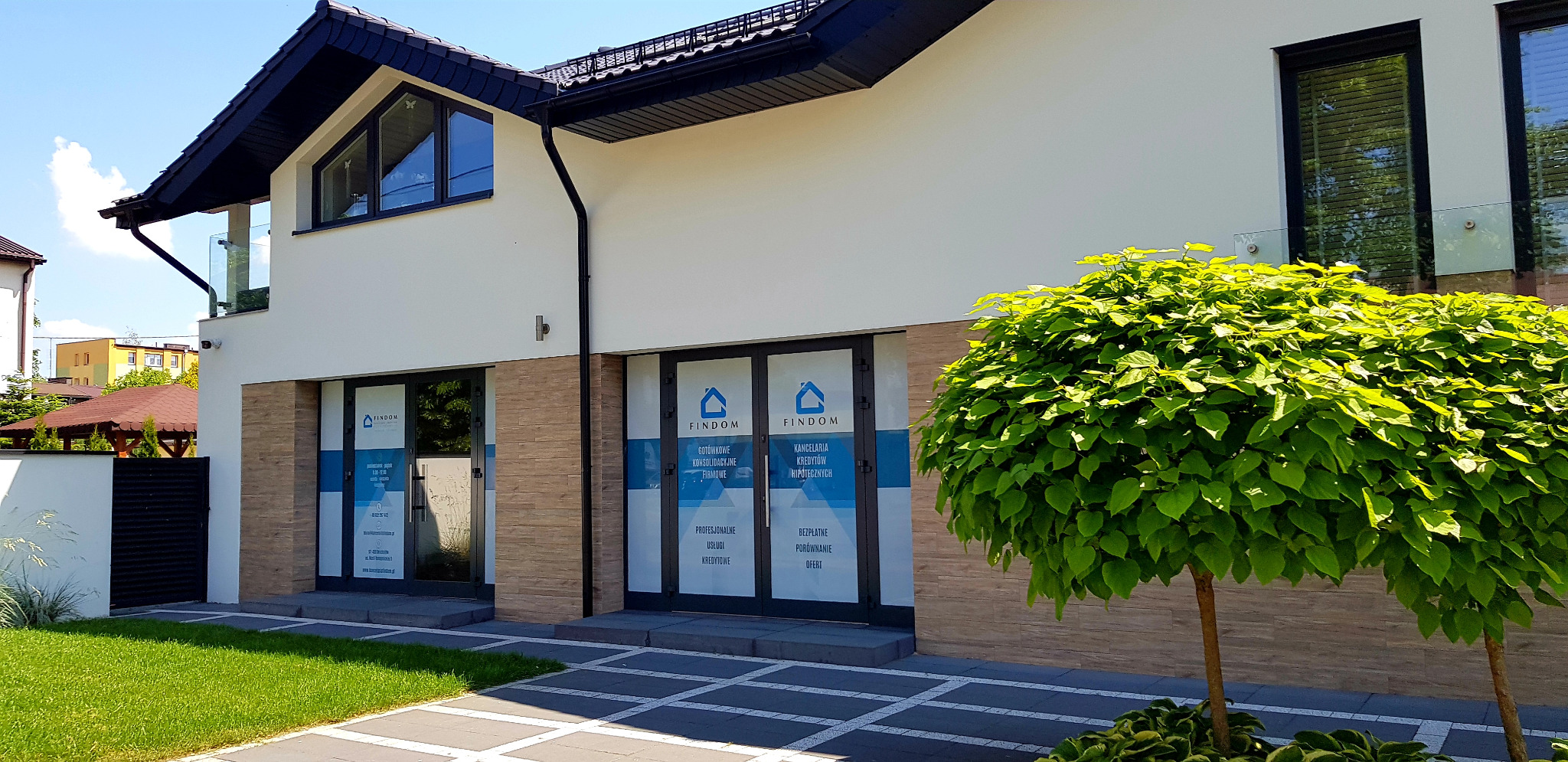 Elewacja biura firmy Findom w Bełchatowie z naklejonymi na szybach informacjami o ofercie: kredyty gotówkowe, konsolidacyjne, firmowe i hipoteczne.