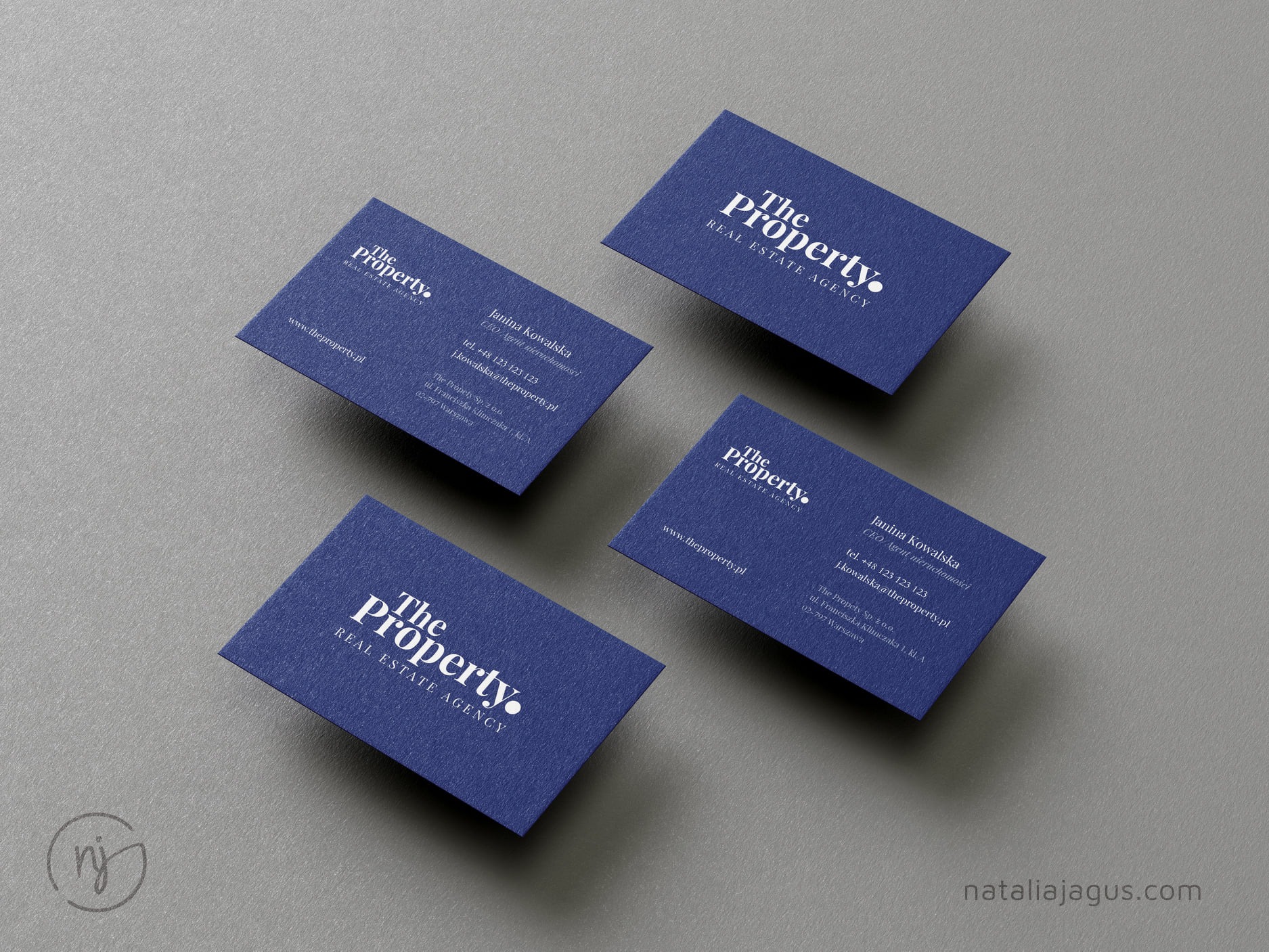 Cztery granatowe wizytówki z białym tekstem „The Property. Real Estate Agency” ułożone na szarym tle, prezentujące dane kontaktowe Janiny Kowalskiej, CEO/Agent Nieruchomości.