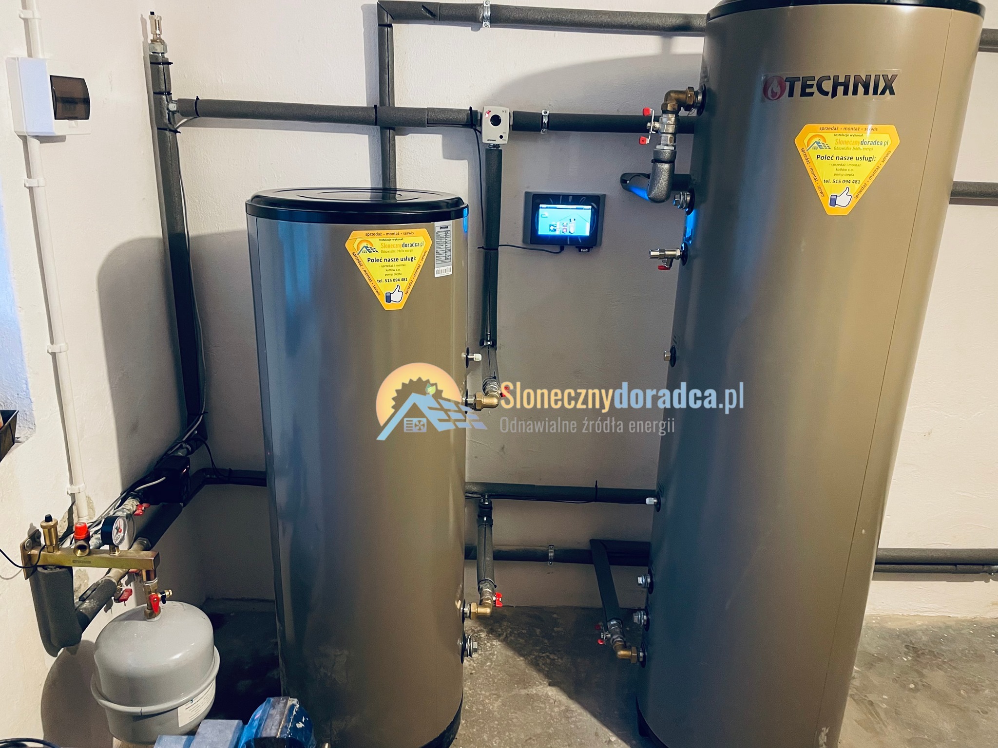 Dwa brązowe zbiorniki buforowe Technix z podłączeniami hydraulicznymi, zamontowane w kotłowni, z widocznym panelem sterowania i fragmentem instalacji rurowej.