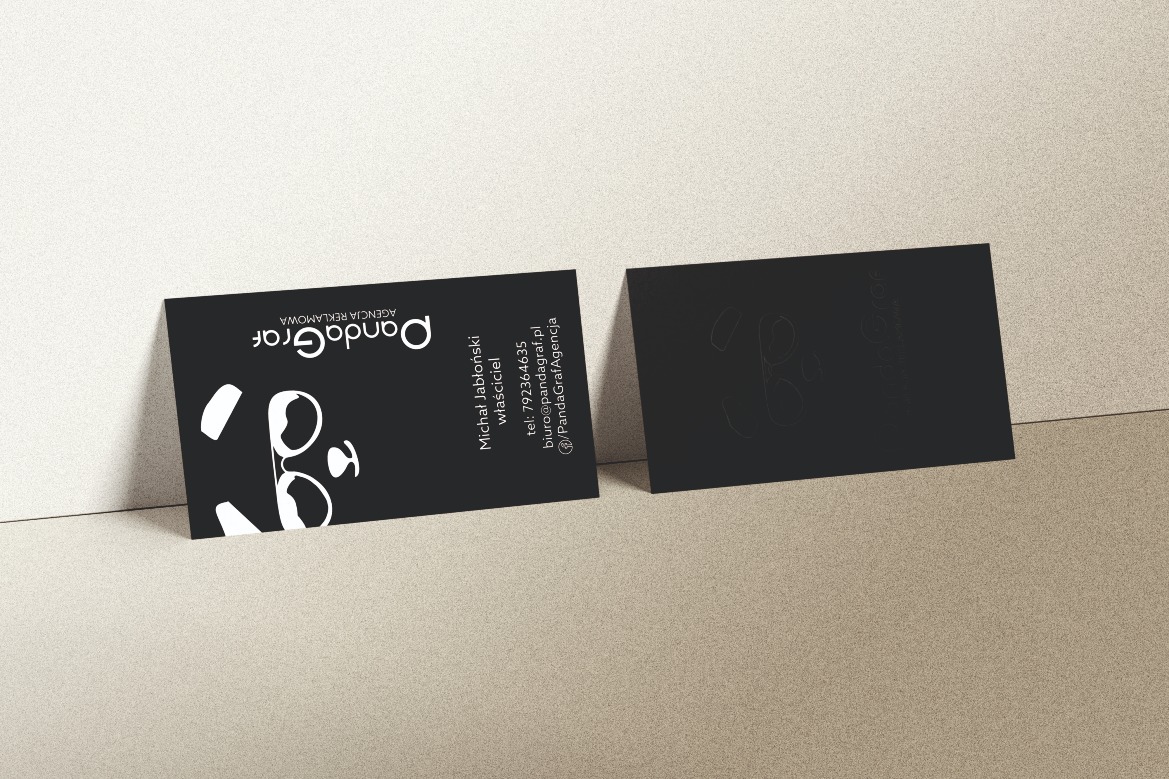 Dwie czarne, matowe karty z logo agencji reklamowej PandaGraf, leżące na beżowym tle. Jedna karta z wyraźnym białym logo i danymi kontaktowymi, druga z delikatnym, wytłoczonym wzorem logo.