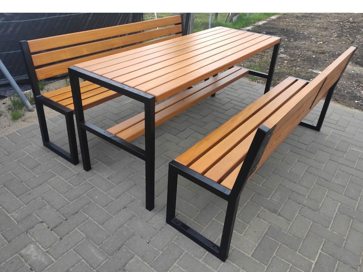Zestaw mebli ogrodowych: stół z drewnianym blatem i dwiema ławkami z oparciami, czarne metalowe ramy, ułożone na szarej kostce brukowej.