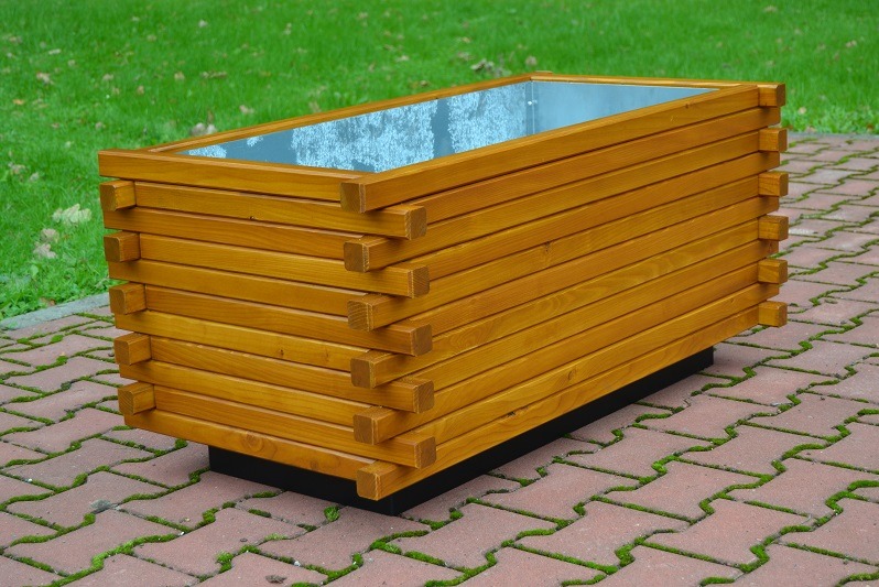 Prostokątna, drewniana donica ogrodowa z metalowym wkładem, ustawiona na kostce brukowej z zieloną trawą w tle.